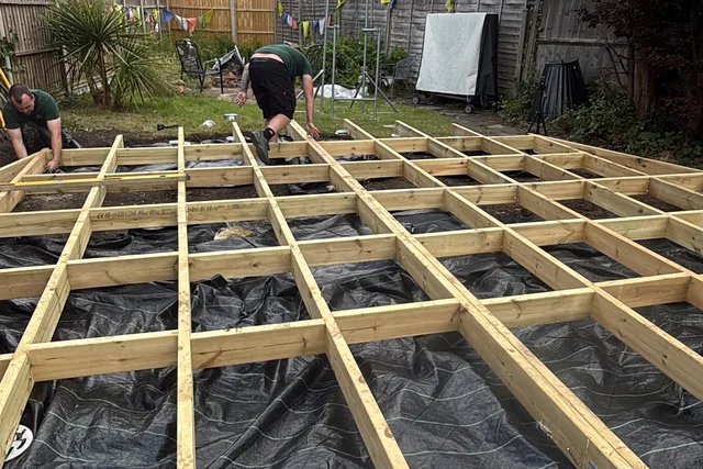Timber floor framing connected above installed ground screws in a landscaped garden.