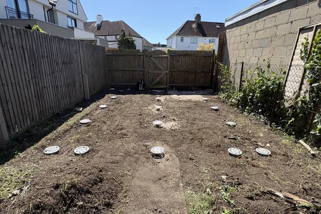 Rows of installed galvanised ground screws across a prepared garden site.