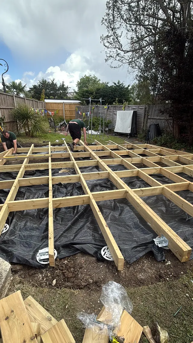 Two installers working around a timber base grid with brackets and screw heads visible below.