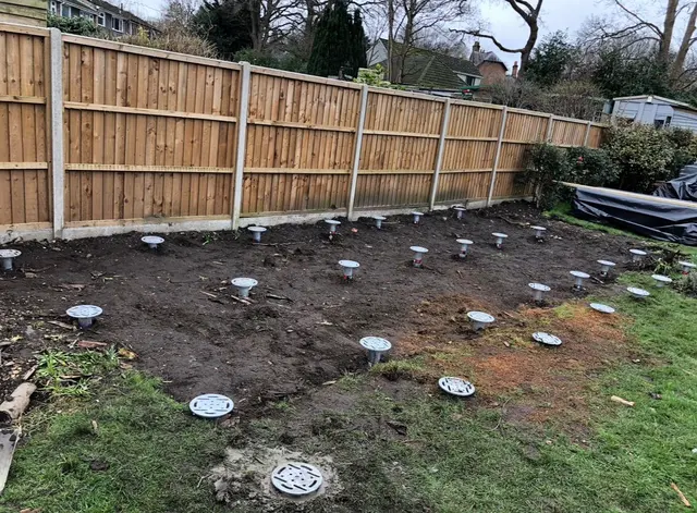 Installed ground screw heads and raised shafts visible in soil inside a fenced garden.