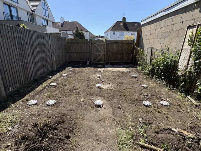 Installed circular ground screw heads distributed across a cleared, enclosed garden footprint.