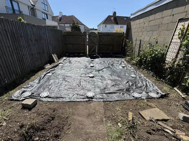 Black ground membrane laid over a garden footprint with ground screw heads left visible.
